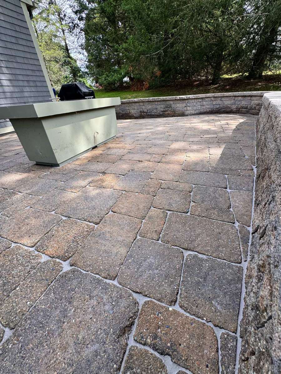 Tan and brown cobblestone paver patio with retaining wall and fresh polymeric sand joints in Rhode Island